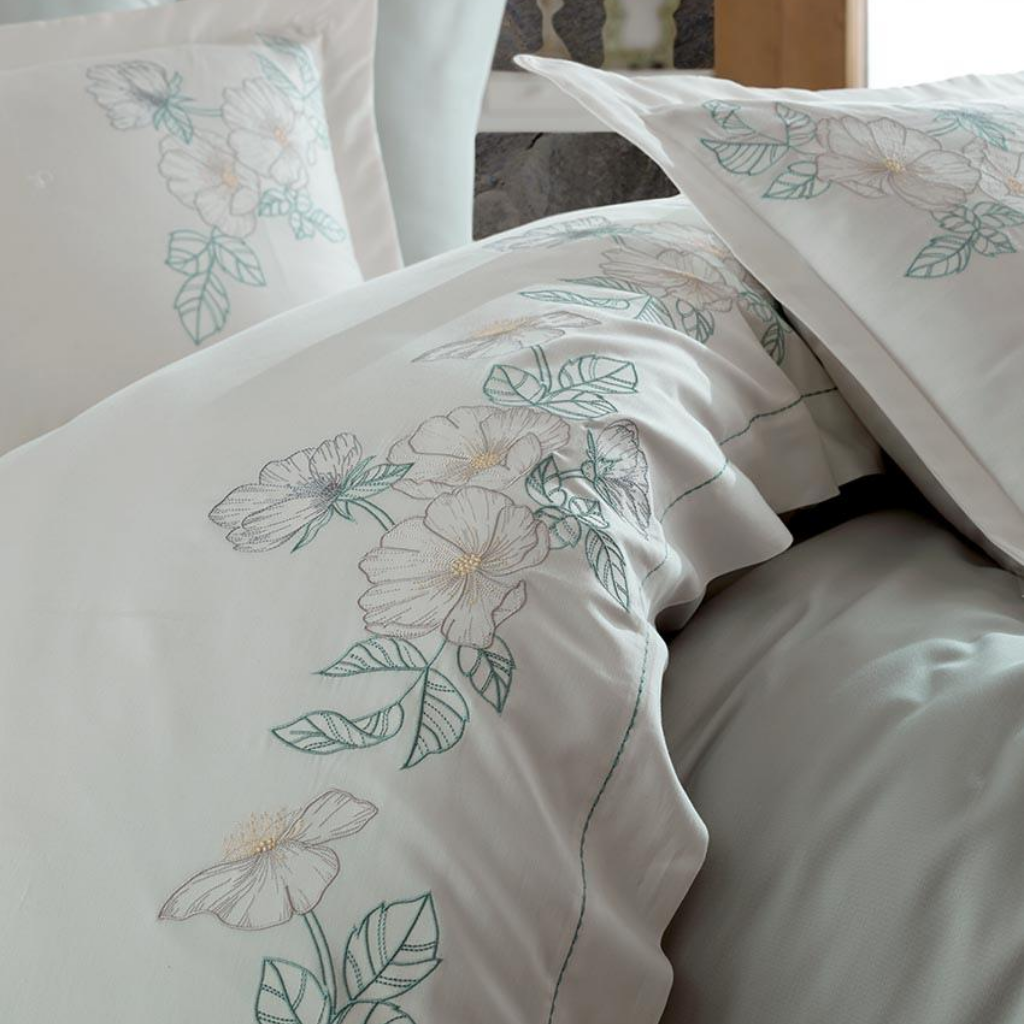Green and grey floral embroideries on white bed cover and pillows