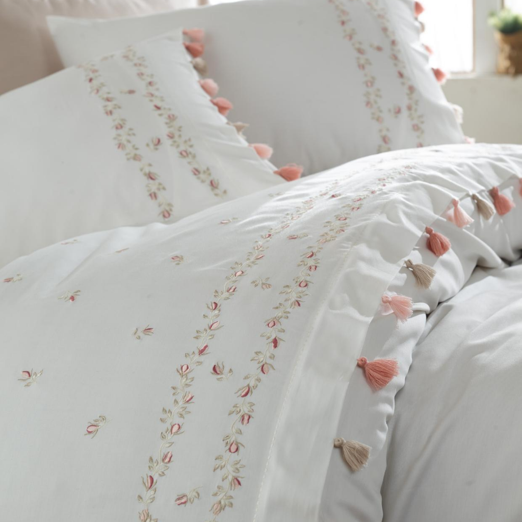White duvet cover and pillows decorated with pink and beige tassels and floral embroideries
